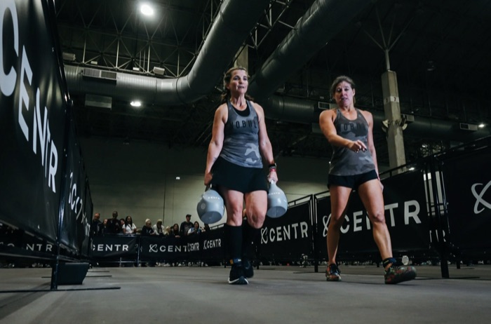 Members carrying kettlebells at a HYROX event